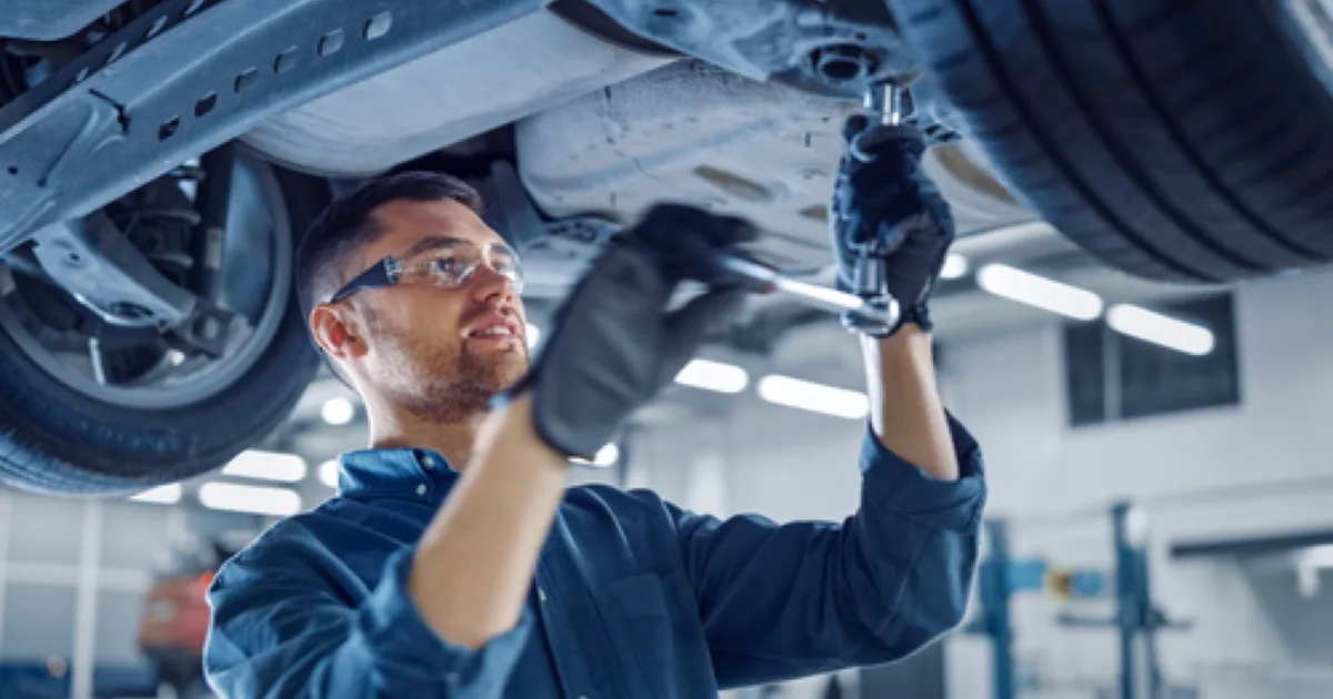 Mechanic inspecting the underside of a car in a modern workshop.