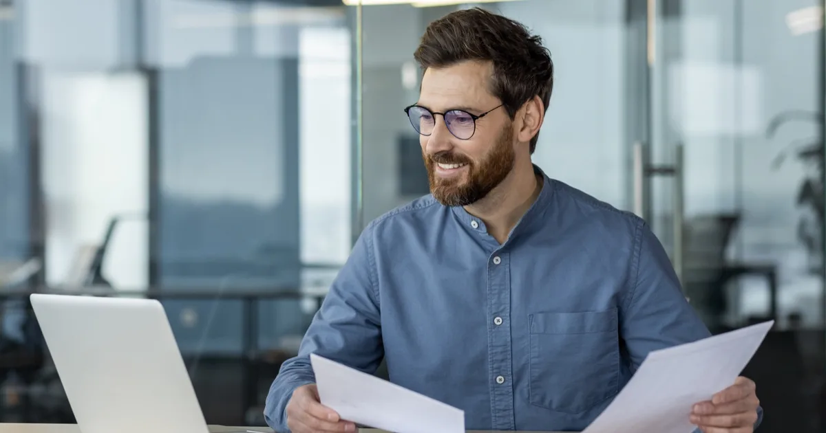 Smiling manager reviewing energy bill paperwork in a modern office.