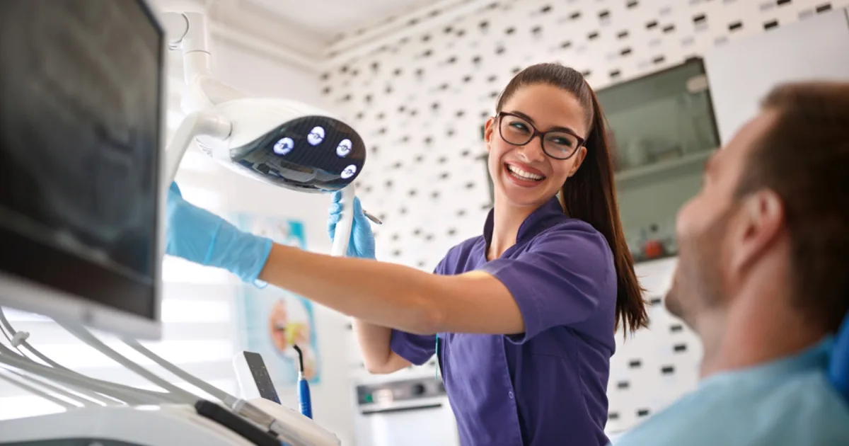 Dental nurse in a bright treatment room with clinical equipment.