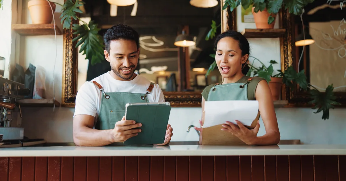 Cafe owners checking orders on a tablet at the counter.
