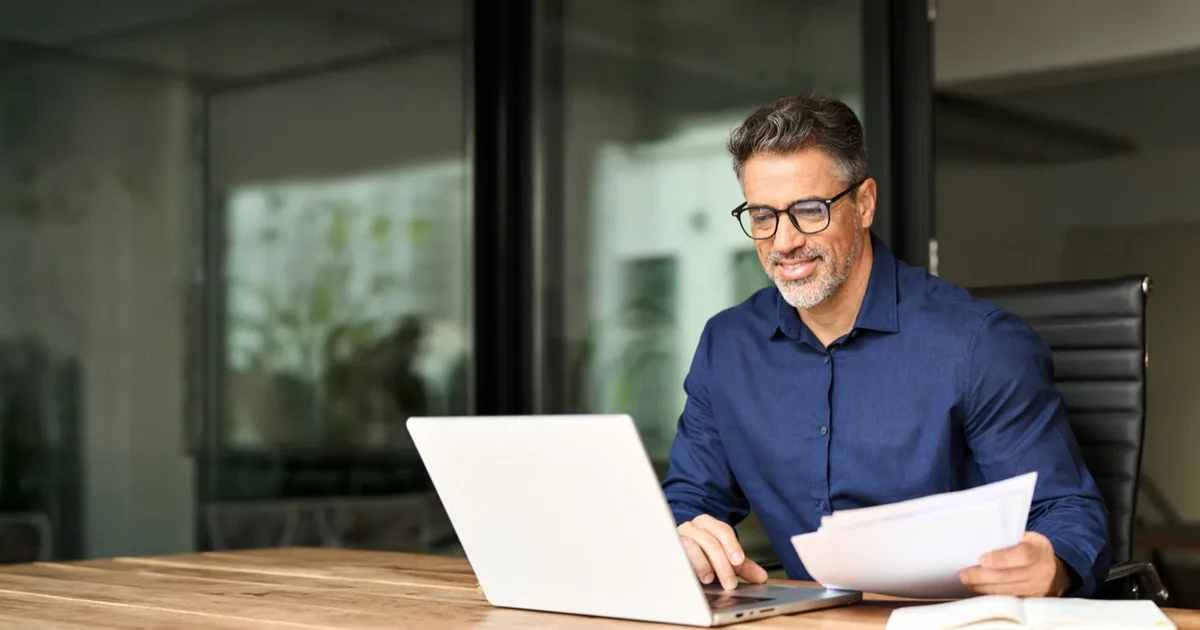 Smiling businessman working with laptop and papers in an office.