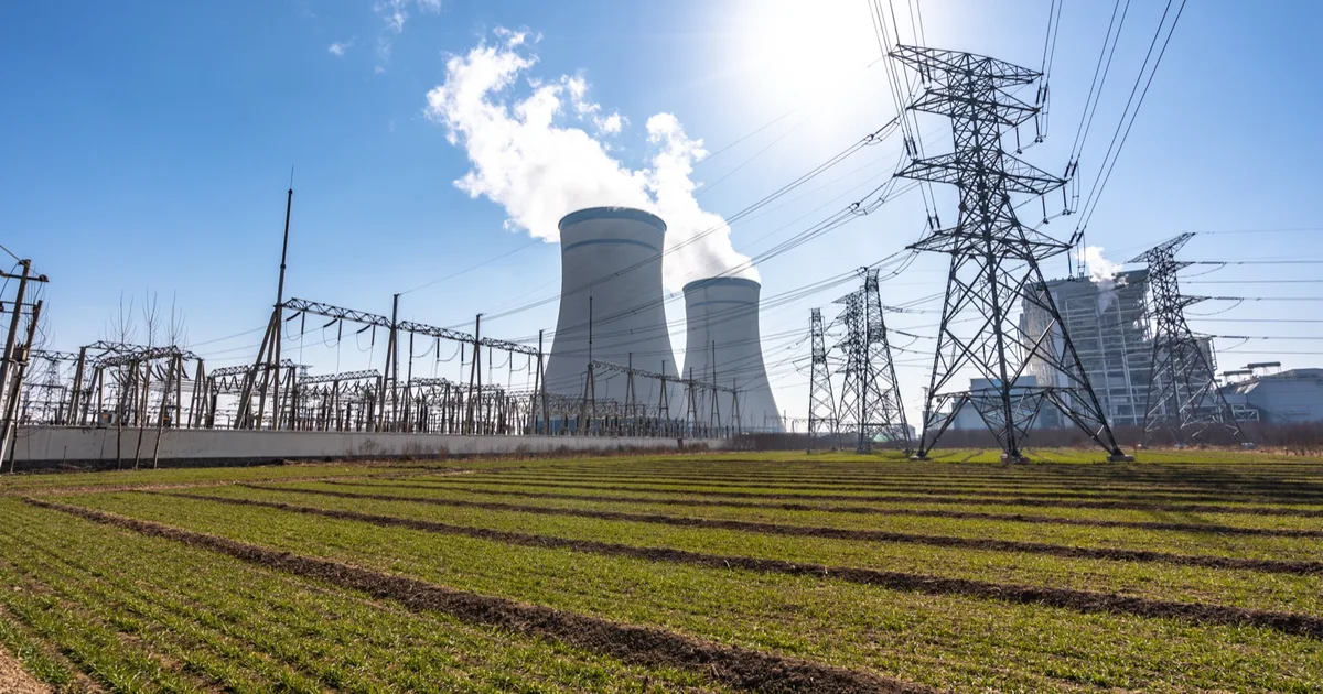 Power station cooling towers and electricity pylons in open countryside.