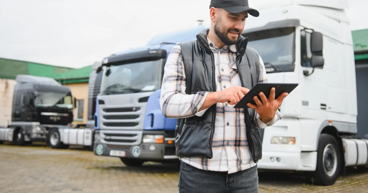 Logistics driver with a tablet in an HGV fleet yard.