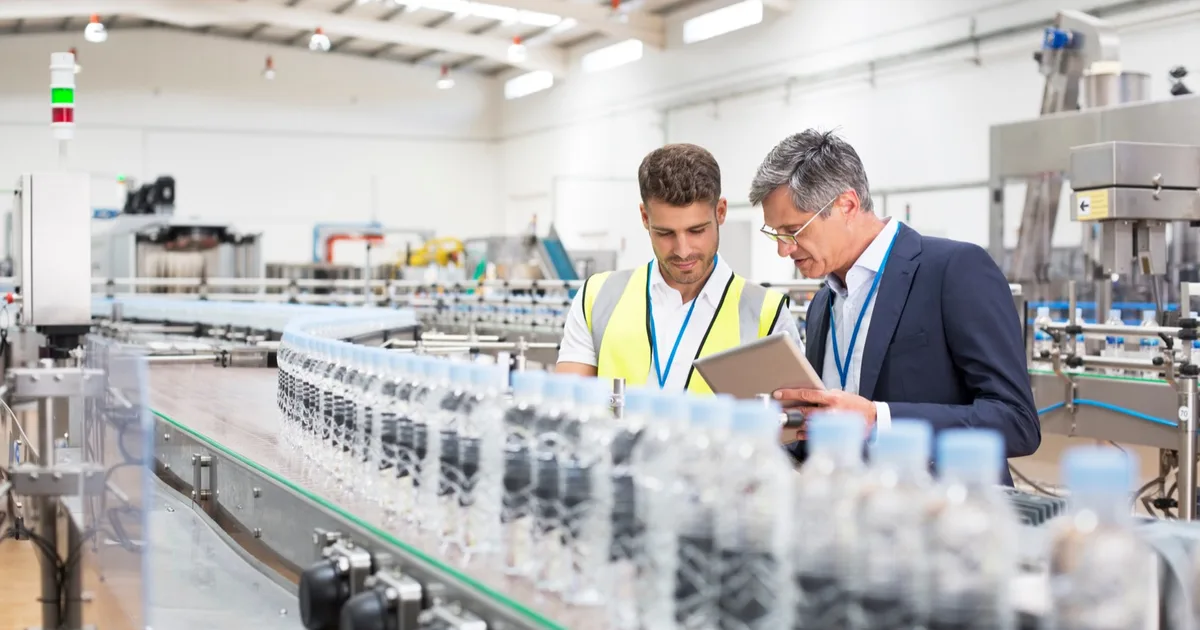 Factory manager and worker reviewing a tablet beside a production line.