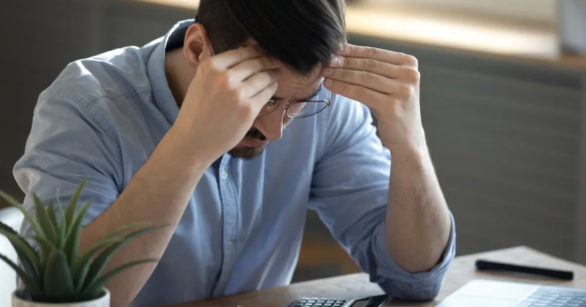 Business owner reviewing bills with a calculator, looking concerned.