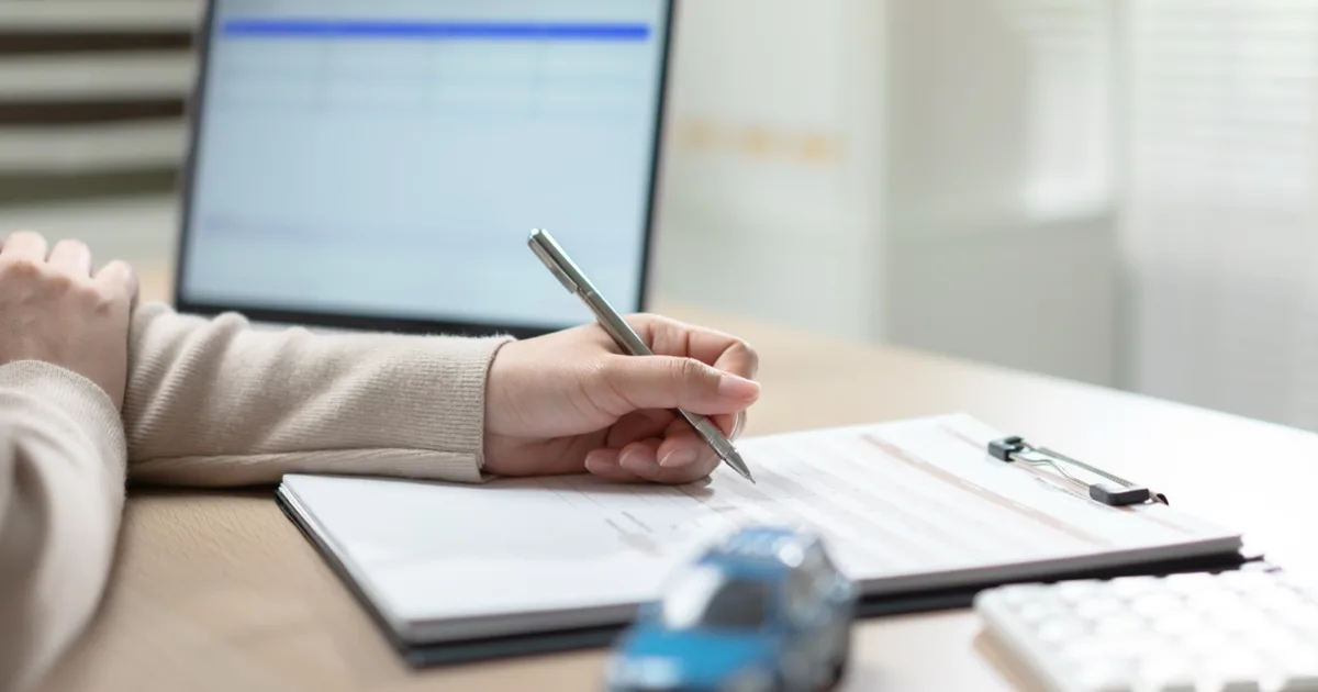 Close-up of a contract being signed on a clipboard at a desk.