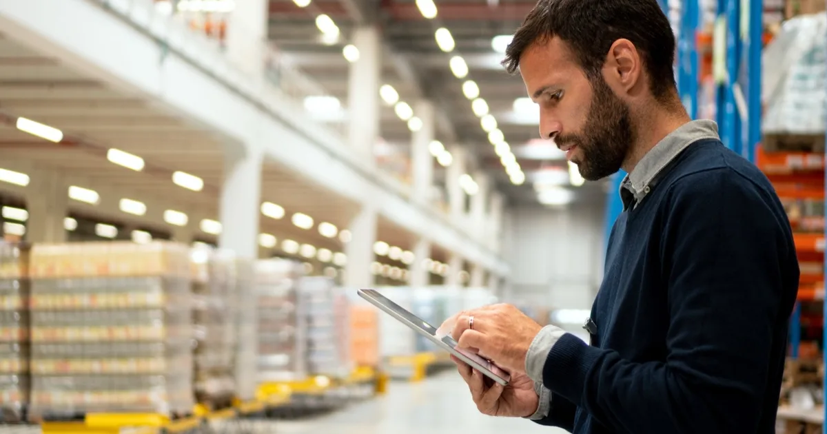 Warehouse worker checking a tablet in an inventory aisle.