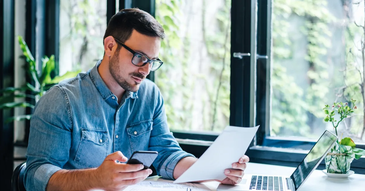 Man cross-checking a bill on his phone and laptop.